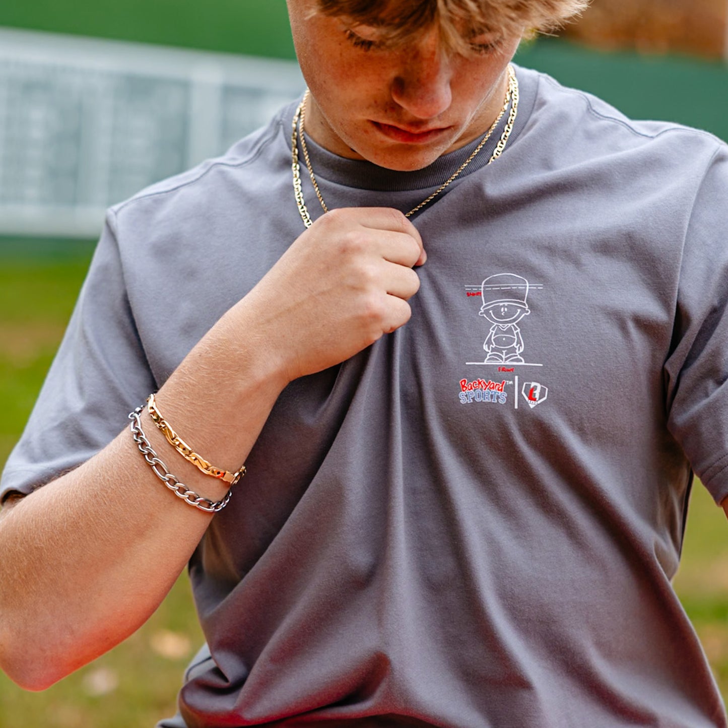 close up of person wearing a gray t-shirt with a Backyard Sports BL101 logo on a sports field