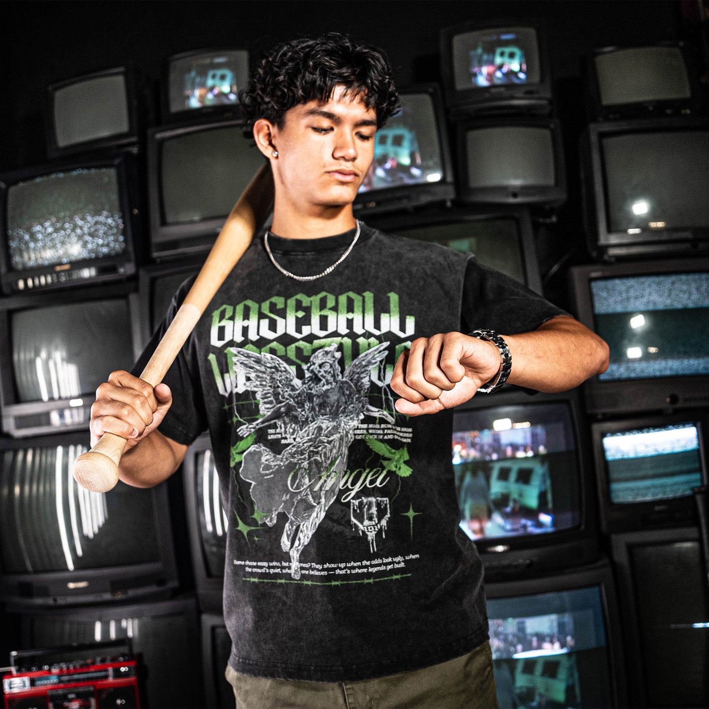 Person wearing green and white graphic tee with text, holding a baseball bat in front of vintage televisions