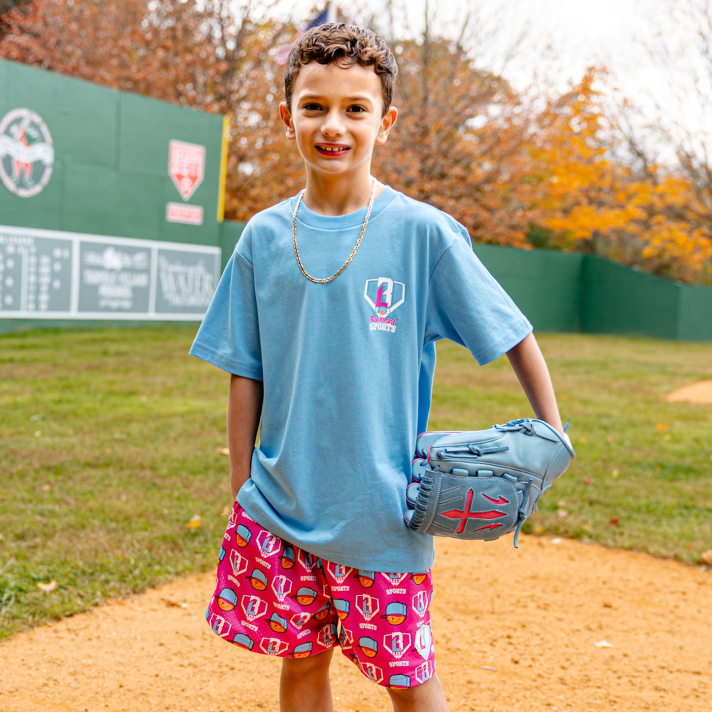 Child wearing a blue Pablo Sanchez t-shirt and pink Pablo Sanchez shorts with a baseball glove on a baseball field.