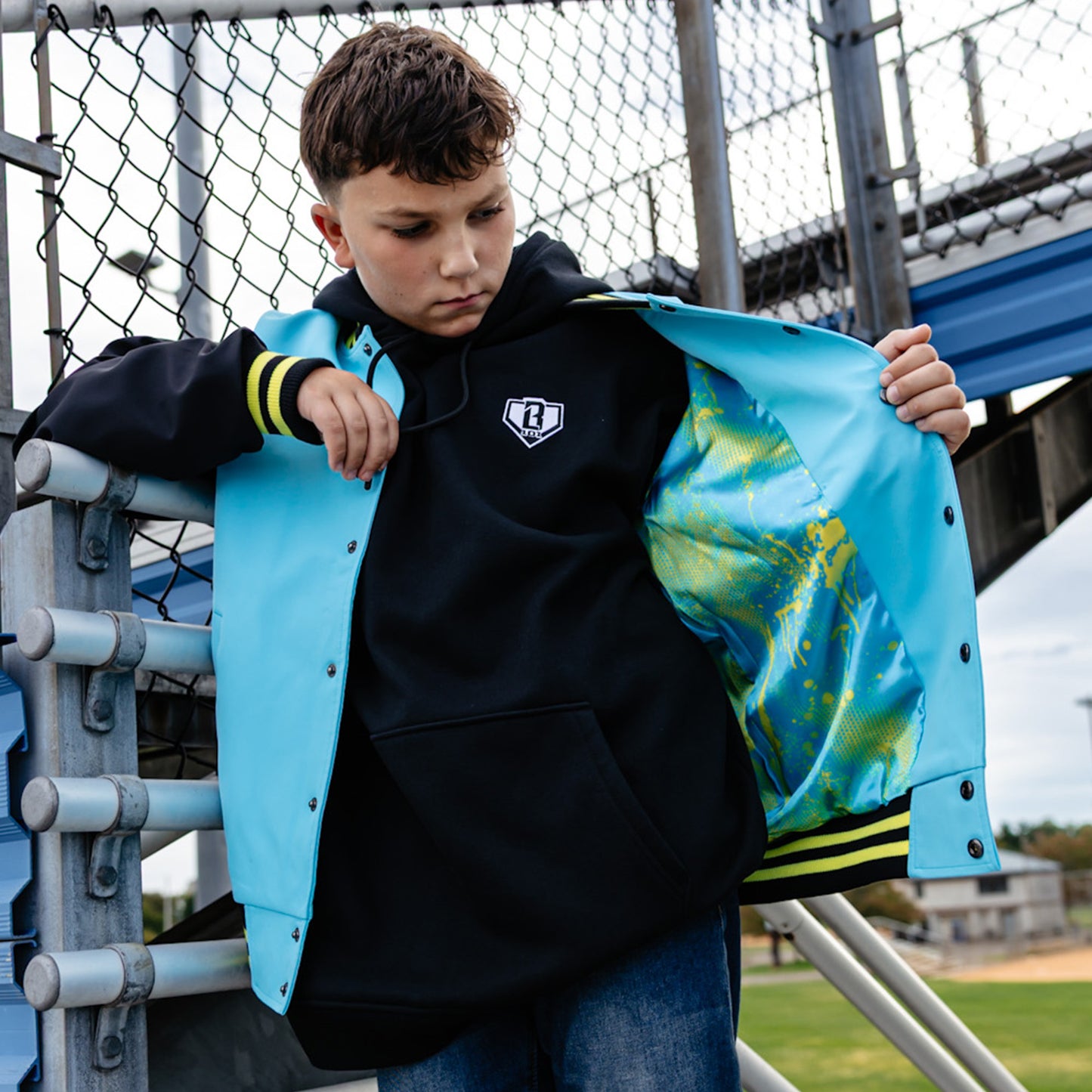 Child holding a blue, black and yellow jacket with a sports field background