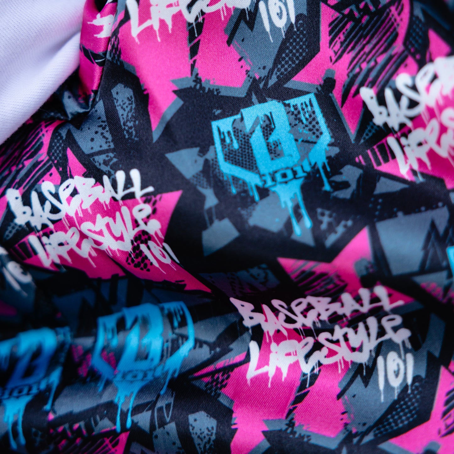 Close-up of a fabric with 'Baseball Lifestyle' and graffiti-style designs on a pink and black background.