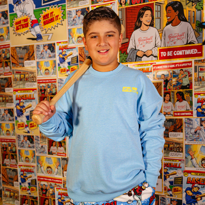 Youth model wearing blue youth crewneck with "Comic Collage" design