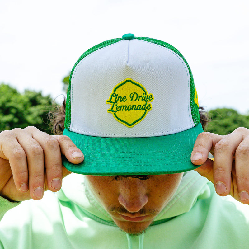 Adult model wearing green hat with "Line Drive Off Field" design