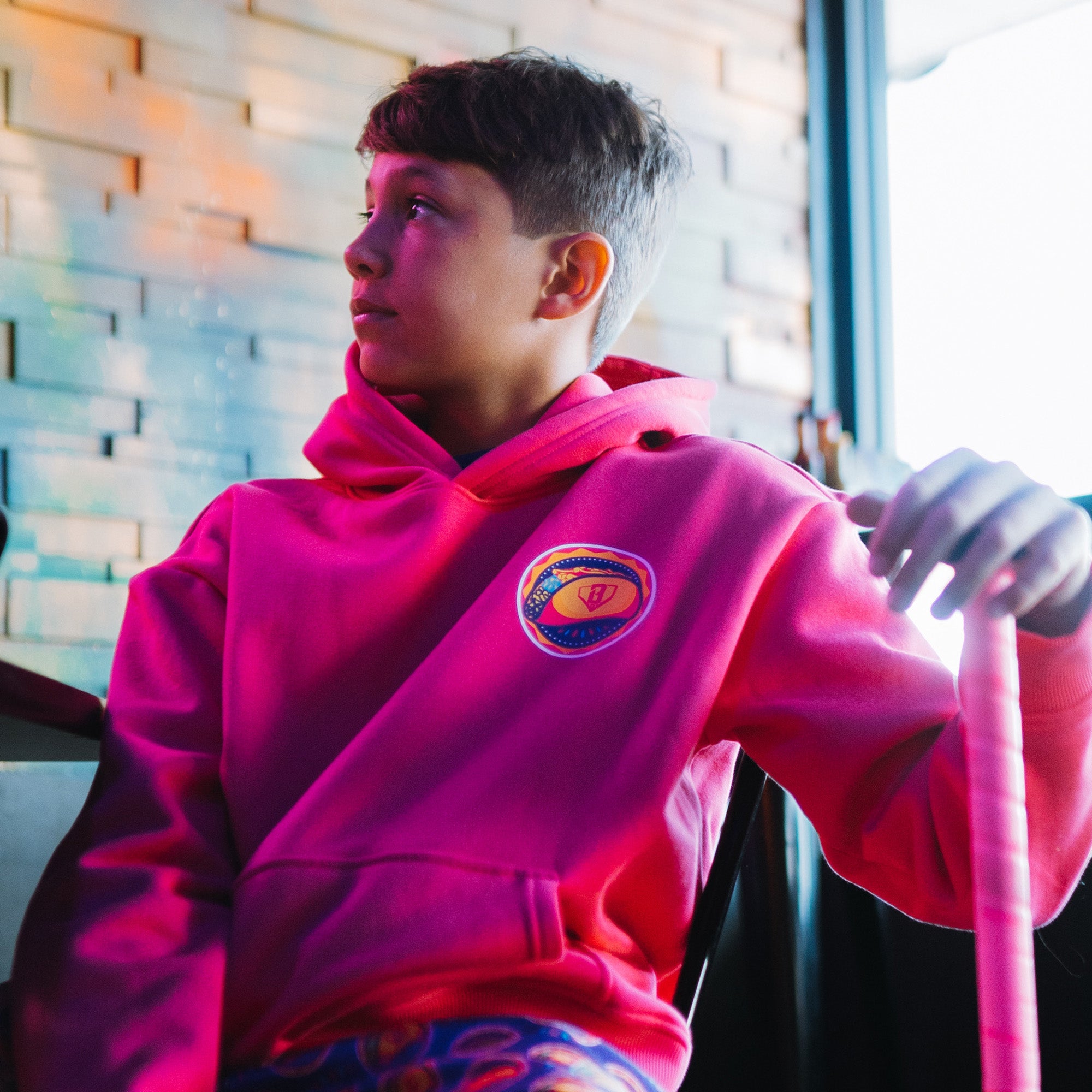 Person wearing a bright pink hoodie with a colorful Taco logo, sitting indoors.