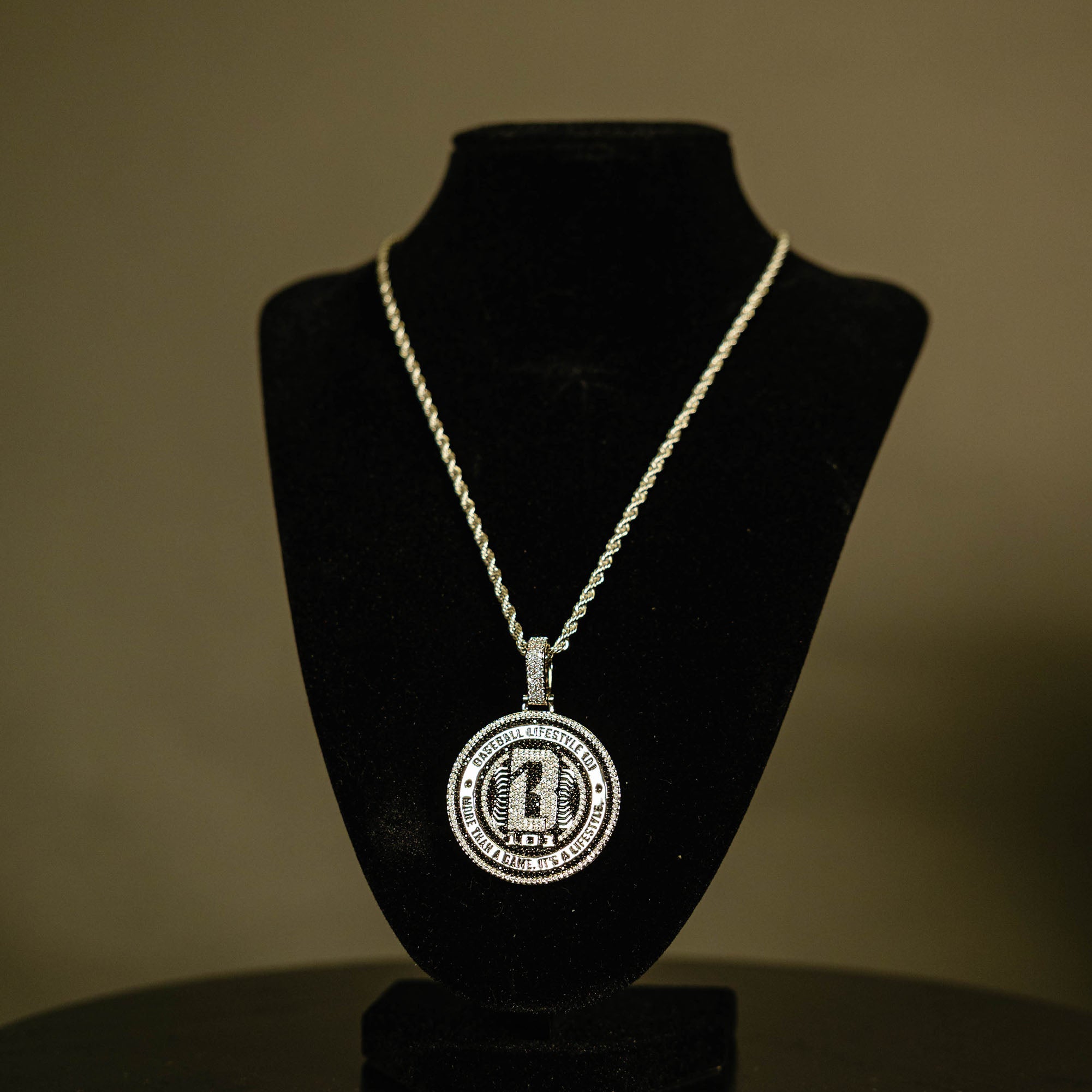 White Gold BL101 Medallion necklace hanging on a display stand against a black background