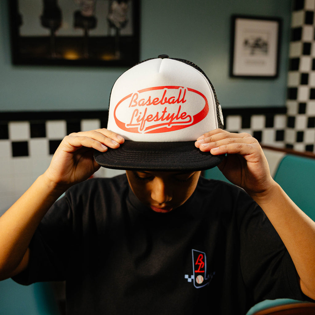Person holding a white and black cap with red 'Baseball Lifestyle' text.