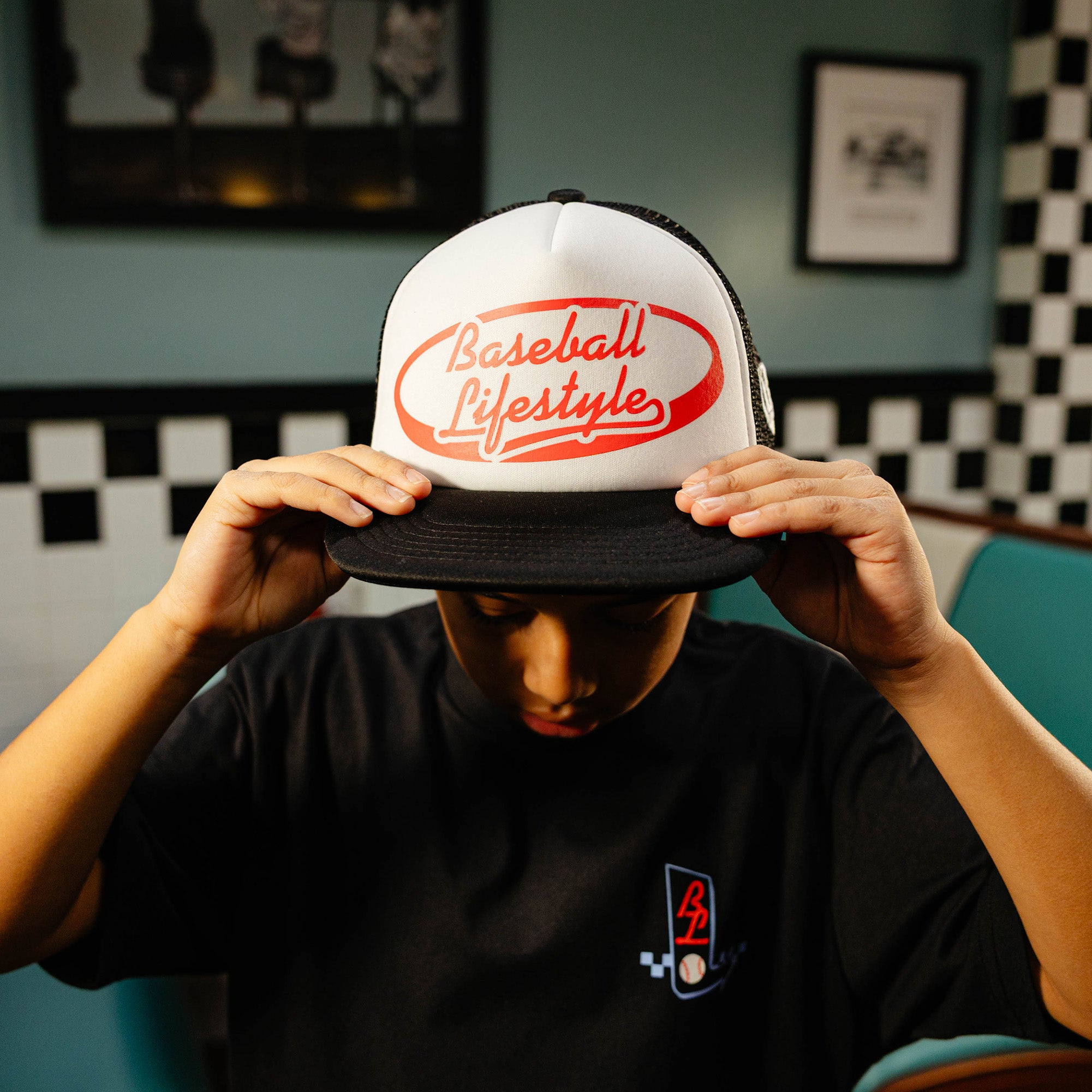 Person holding a white and black cap with red 'Baseball Lifestyle' text.
