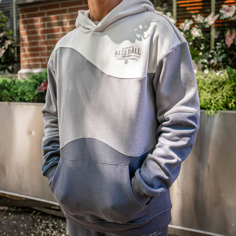Person wearing a 3 toned gray hoodie with 'Authentic Baseball Lifestyle PREMIUM APPAREL' text, standing outdoors.