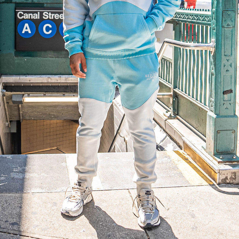 Person wearing light blue and white color-blocked sweatpants in front of subway entrance