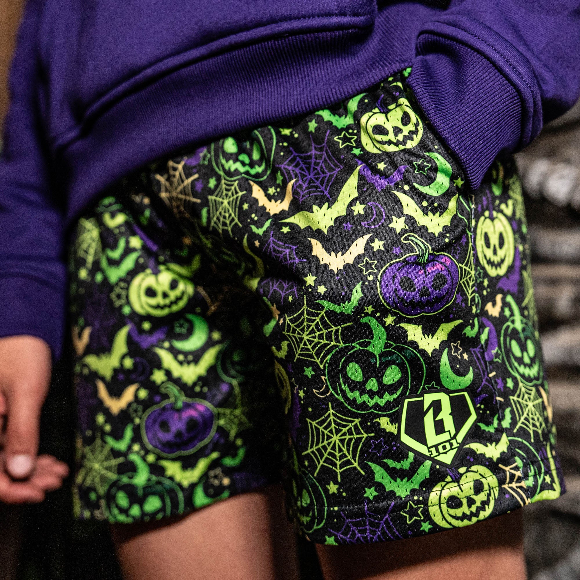 Person wearing a purple hoodie and Halloween-themed shorts with pumpkins, ghosts, and bats.