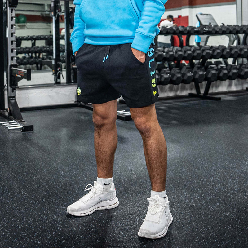 Person wearing a blue sweatshirt, black shorts with BL101 text, and white sneakers in a gym setting.