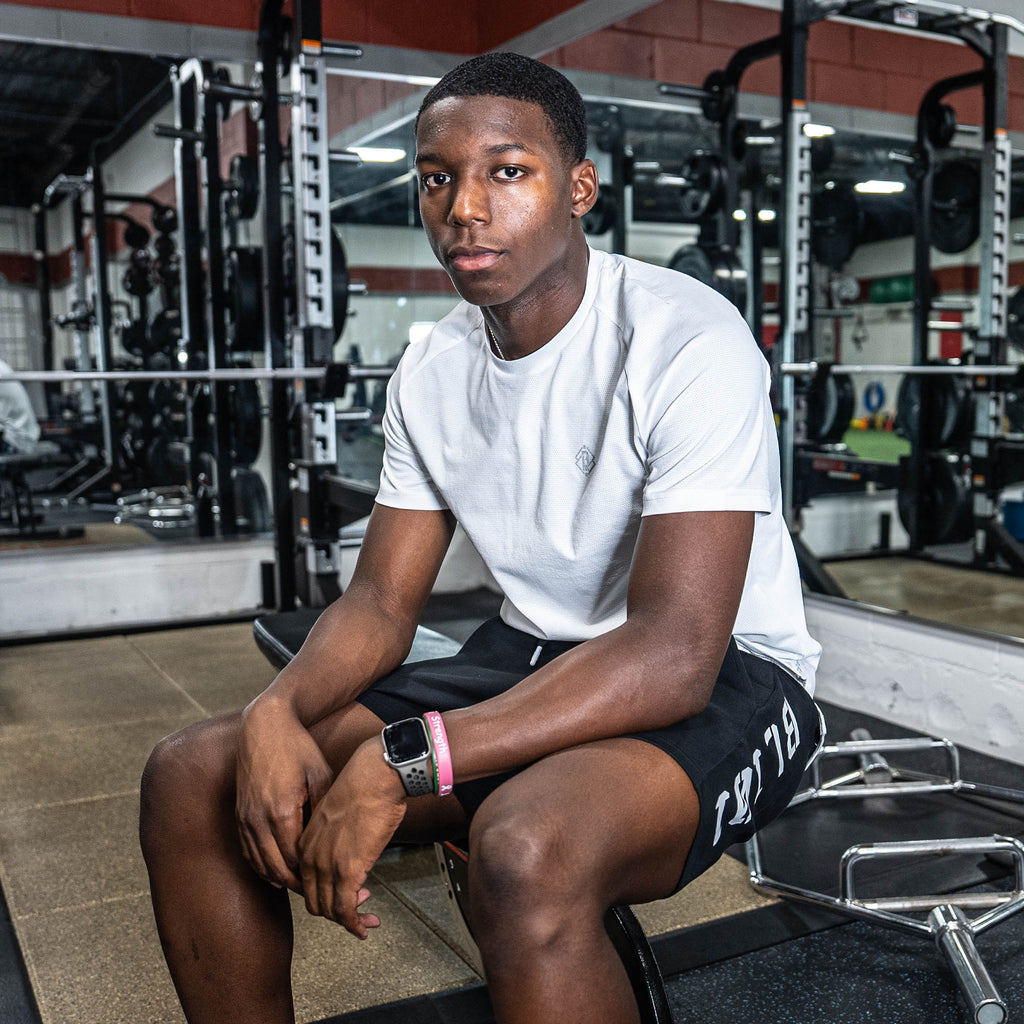 Person sitting on a weight bench in a gym in white BL101 t shirt and black BL101 shorts