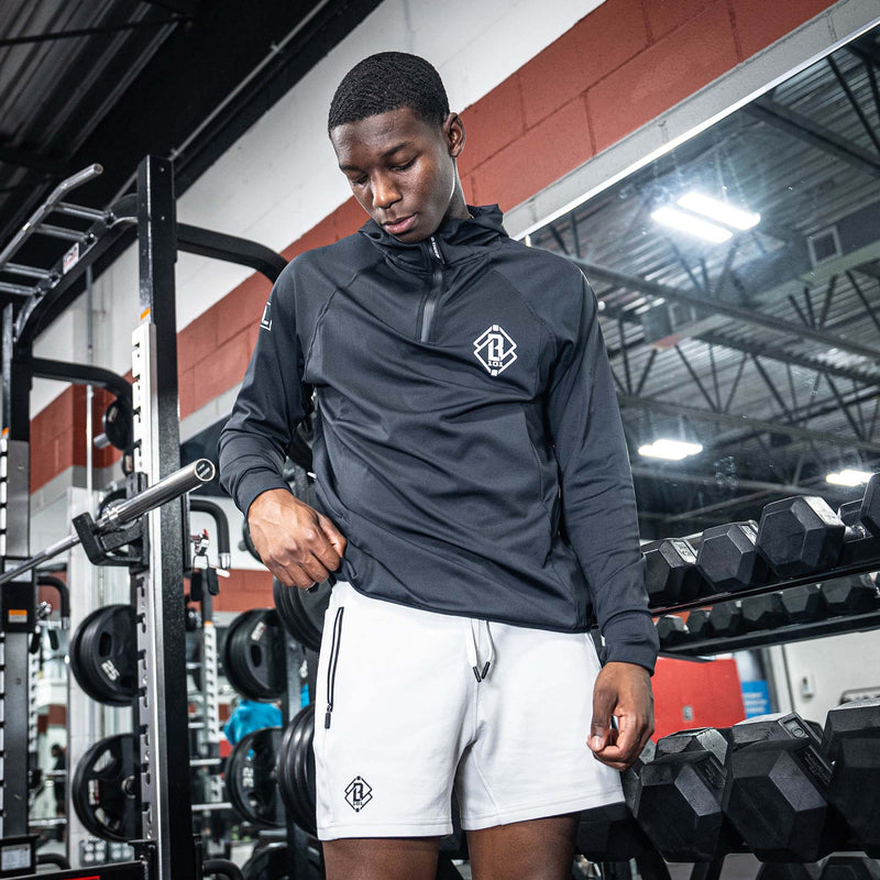 Person wearing a black jacket with white BL101 logo and white shorts with black BL101 logo in a gym setting