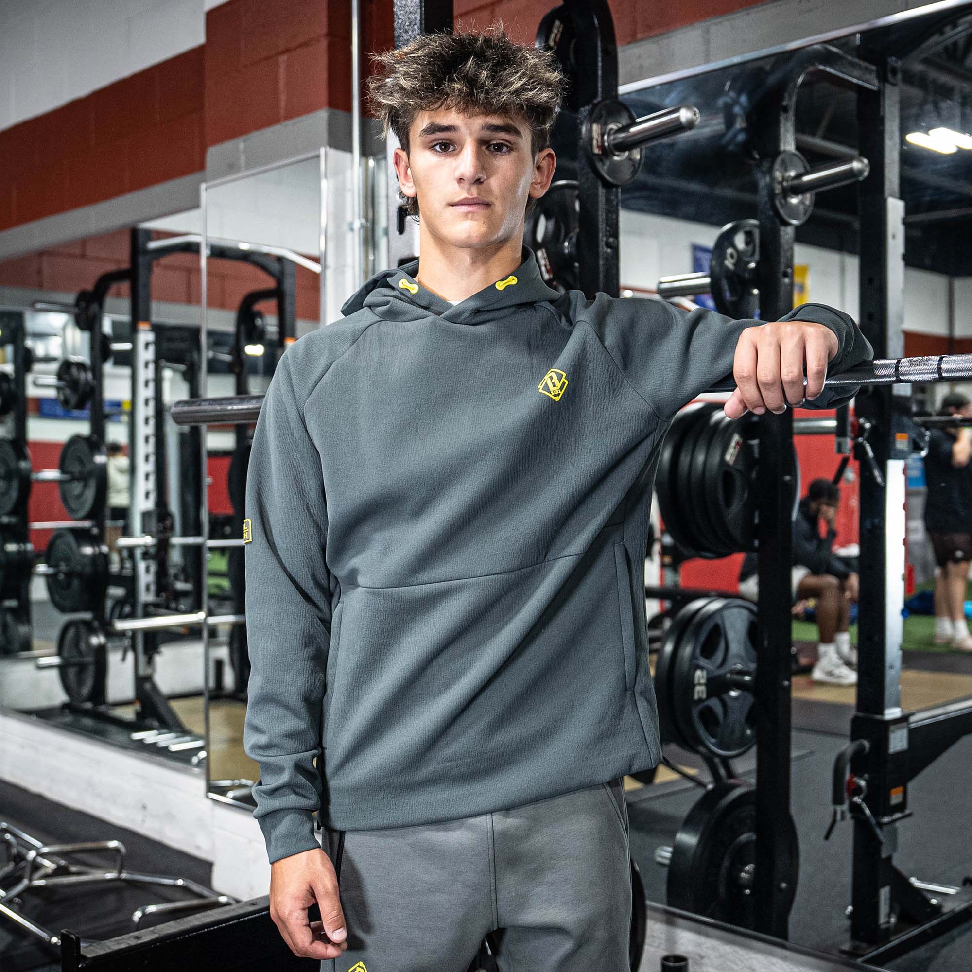 Person wearing a gray hoodie with a yellow BL101 logo in a gym setting