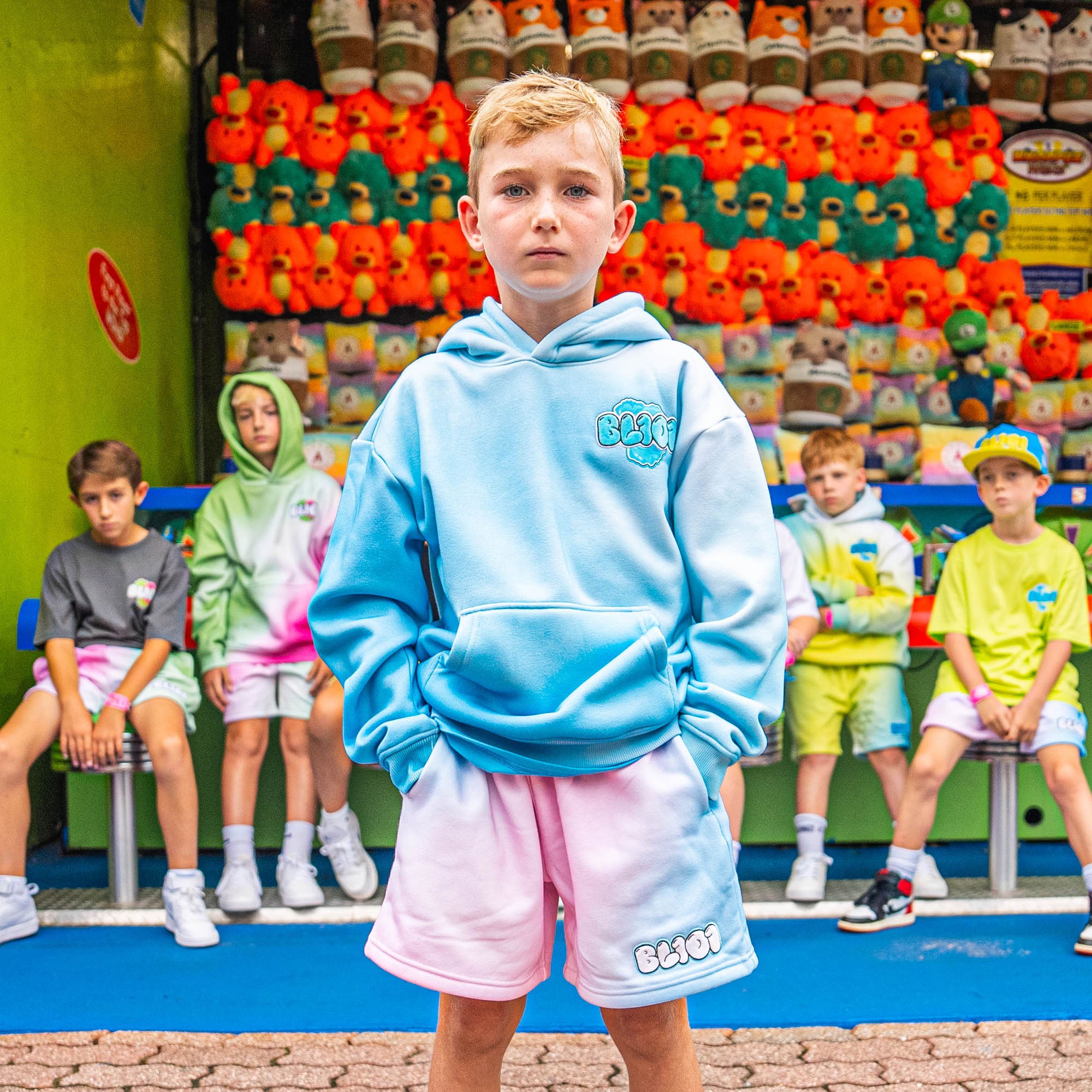 Child wearing a light blue hoodie and pink shorts with BL101 logo standing in front of colorful toy display