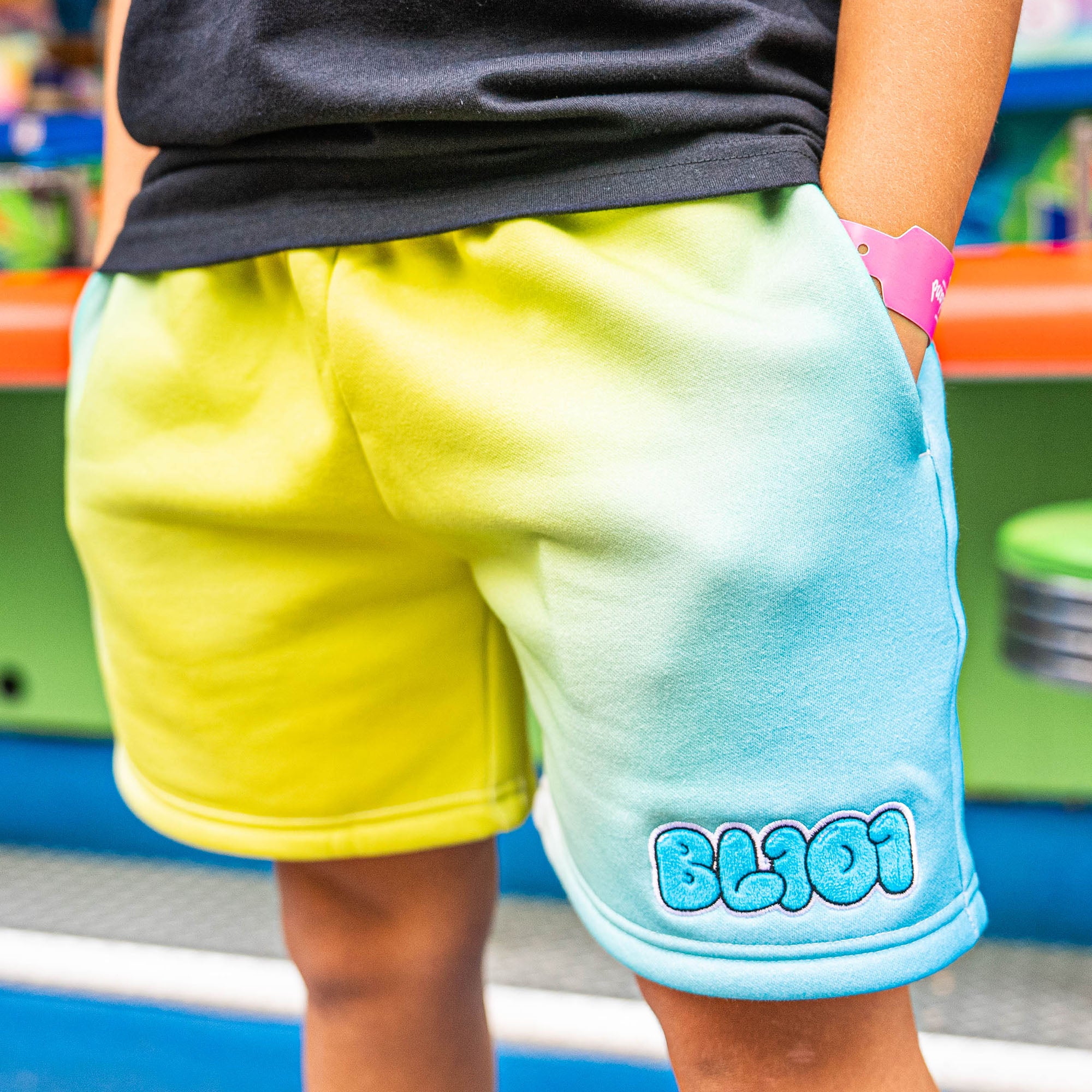 Person wearing yellow and blue shorts with 'BL101' branding, standing in front of a colorful background.