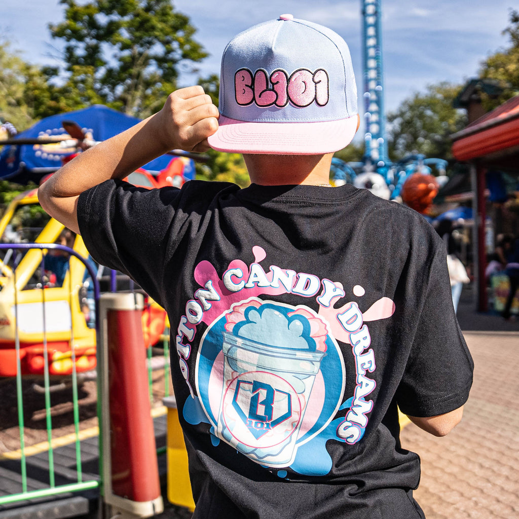 Person wearing a black t-shirt with 'Cotton Candy Dreams' design and a cap in an amusement park setting.