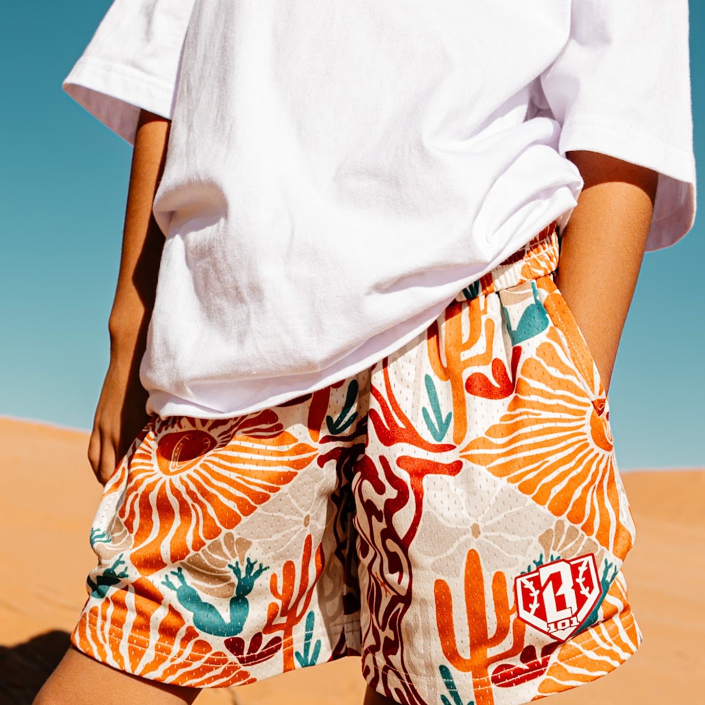 Person wearing colorful cactus and desert patterned shorts with a white shirt against a clear blue sky.