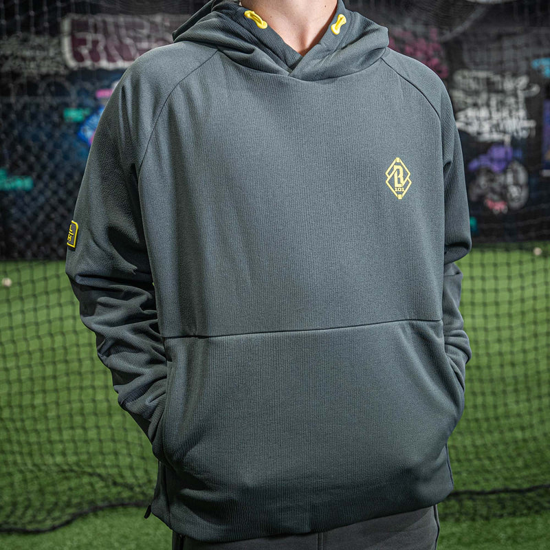 Person wearing a gray hoodie with a yellow BL101 logo in front of a sports net.