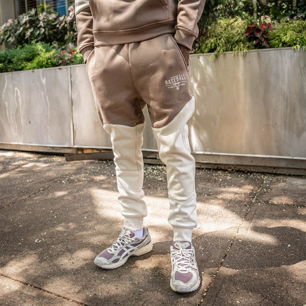 Person wearing a brown and beige tracksuit with 'Baseball Lifestyle 101' text on a concrete surface.