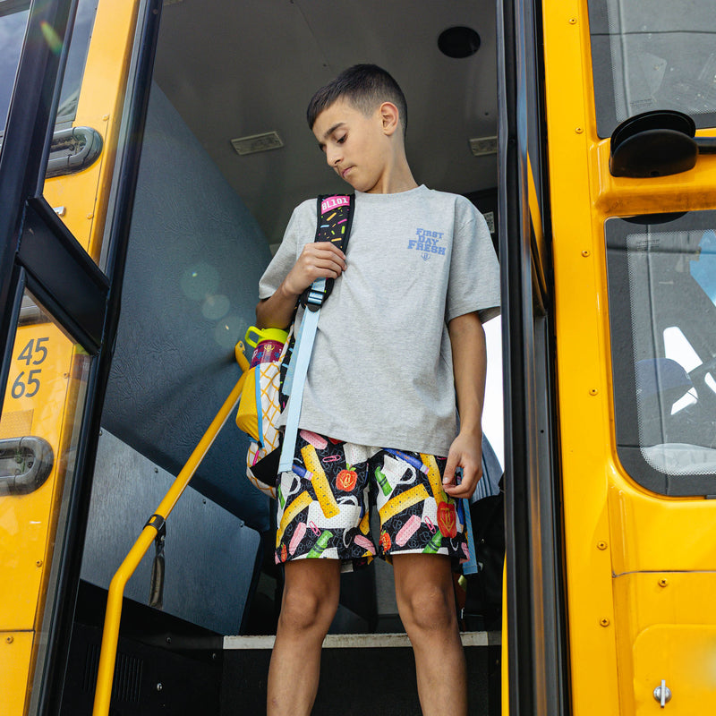 Youth model wearing multi-color youth shorts with "First Day Fresh Youth" design