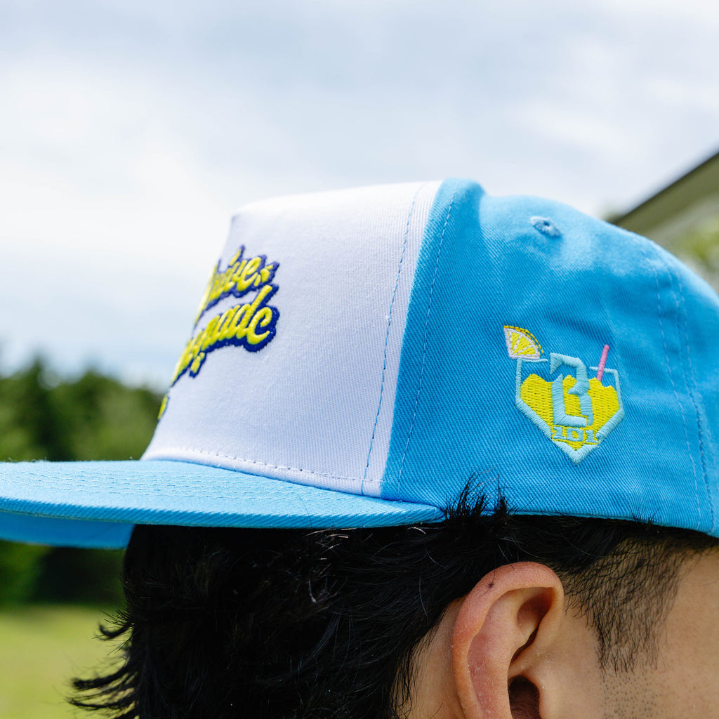 Adult model wearing blue hat with "Lemonade Off Field" design