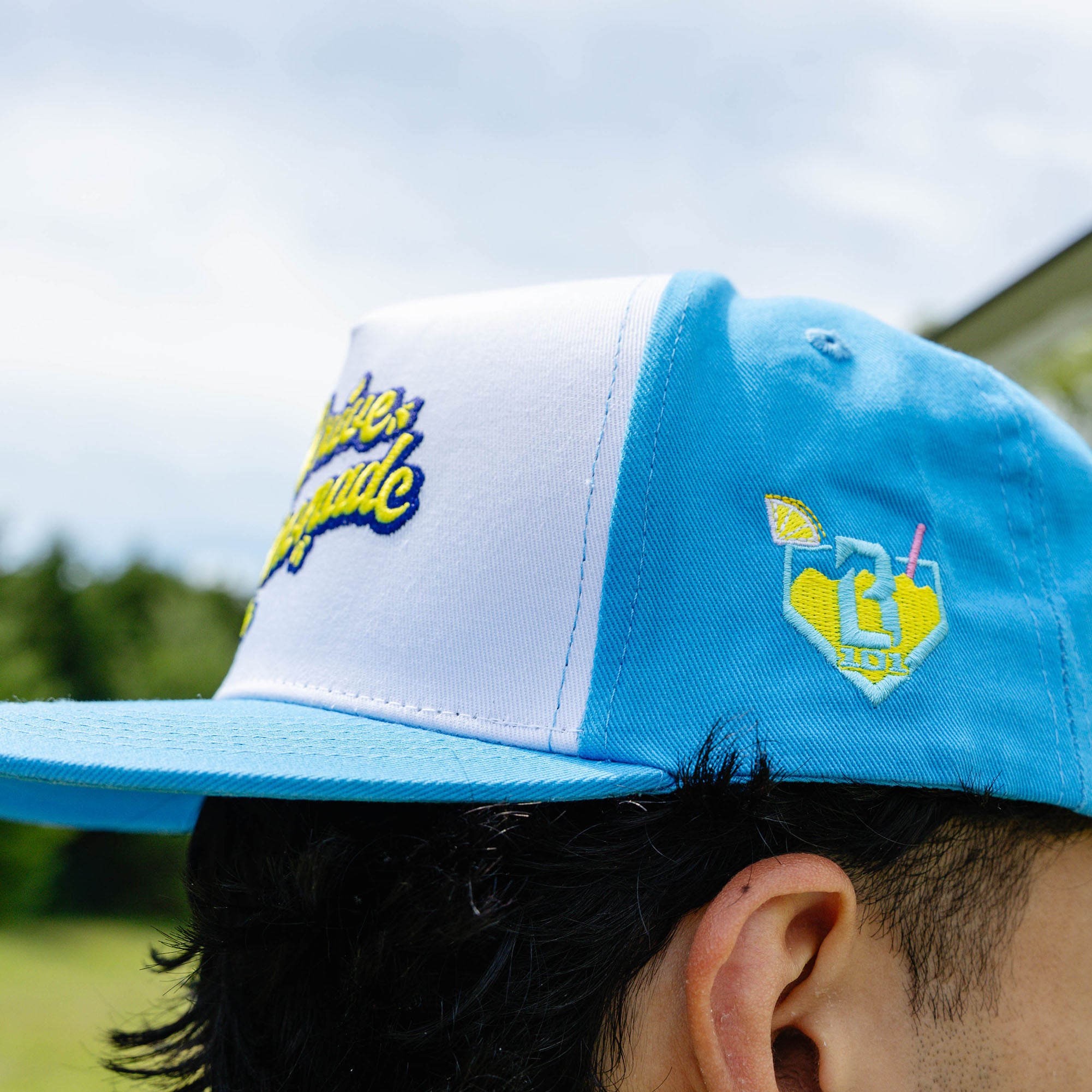 Adult model wearing blue hat with "Lemonade Off Field" design
