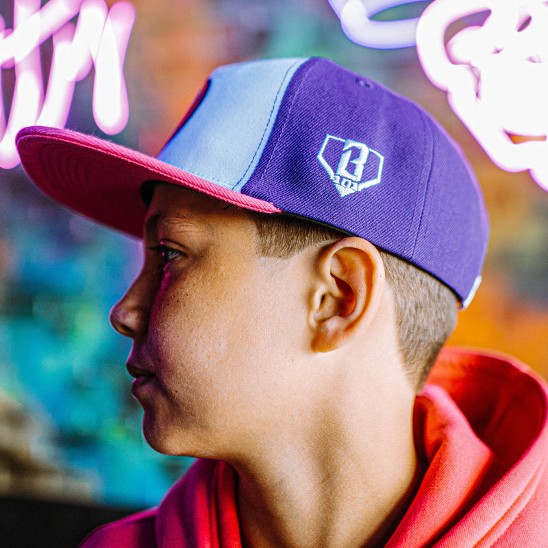 Person wearing a pink and purple cap with a white BL101 logo, standing against a vibrant background.
