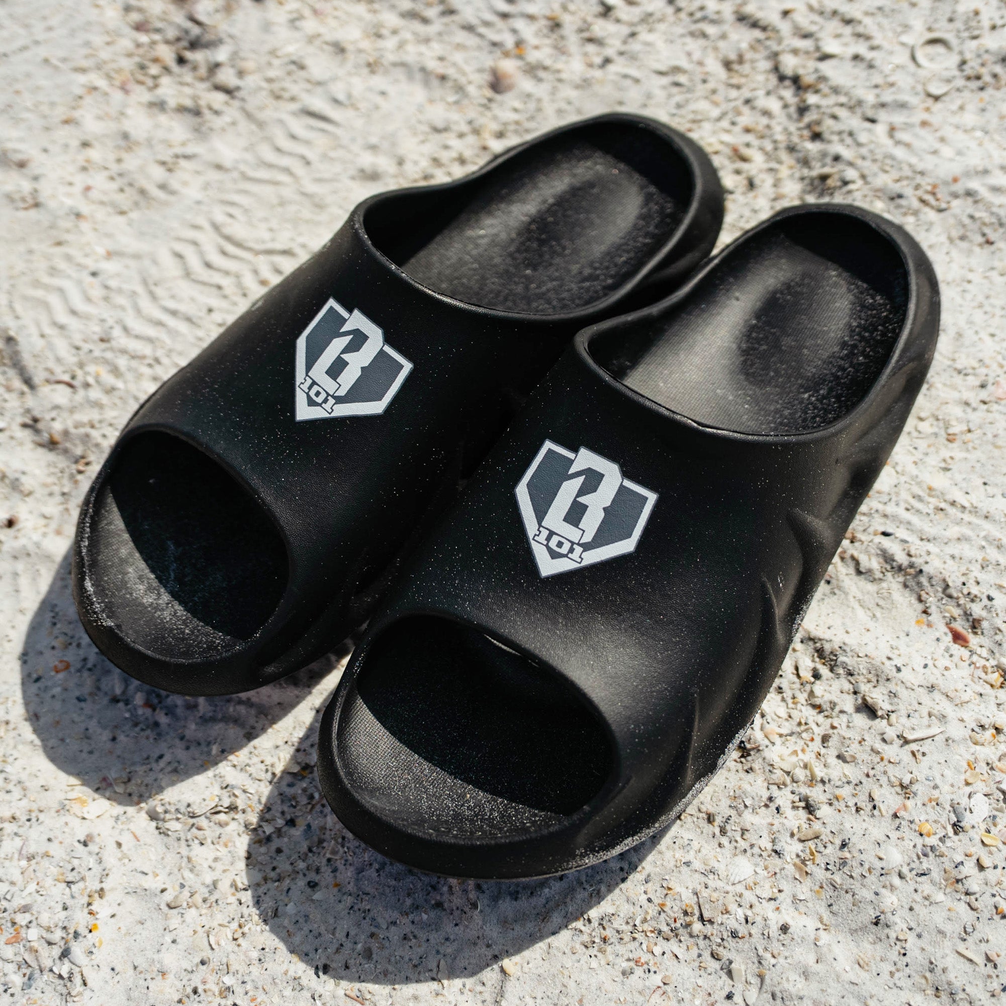 Angled shot of BL101 black slides on a white concrete pedestal with the BL101 logo visible on the strap.