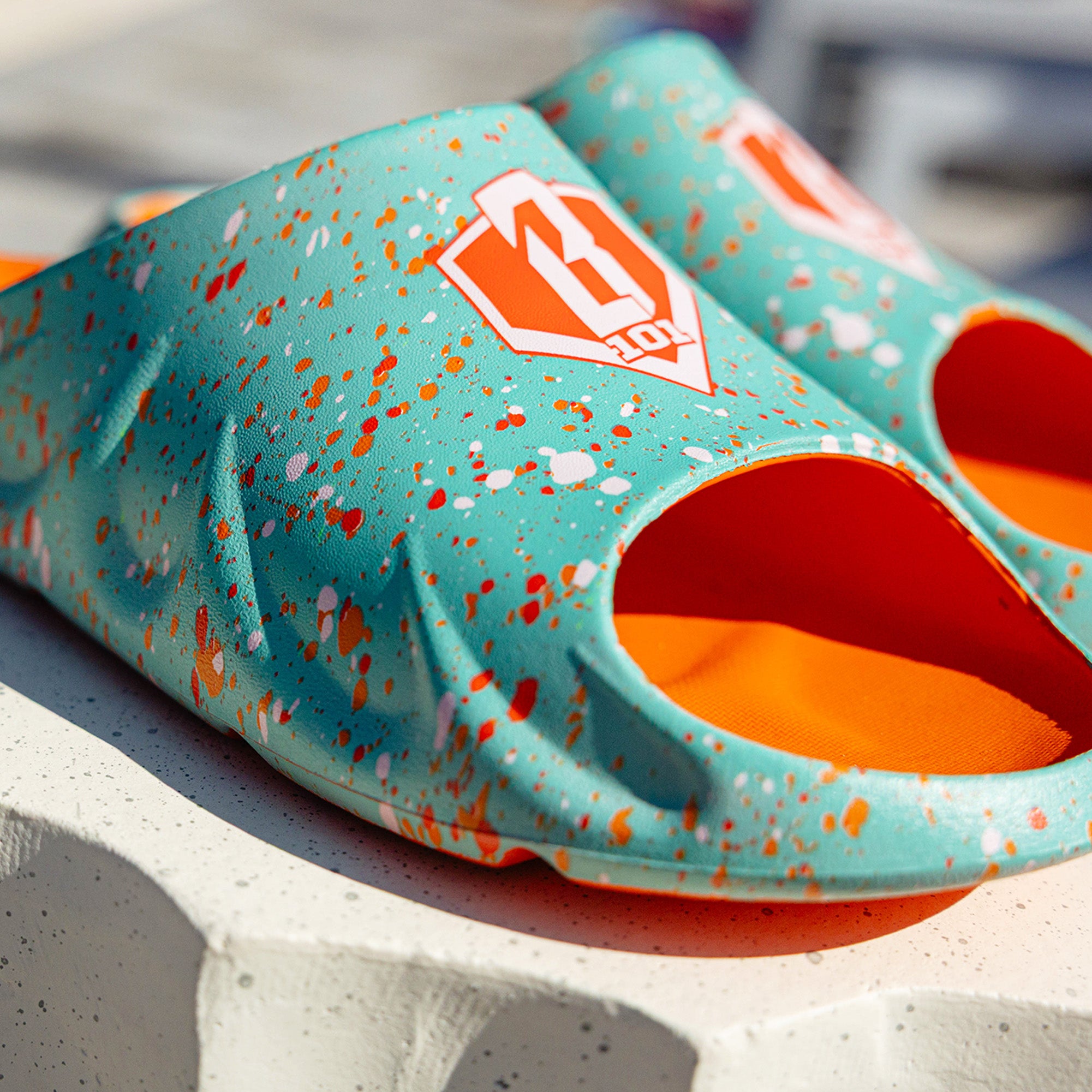 Close-up of BL101 teal splatter print sandal showing the orange and white BL101 logo and textured sole detail.