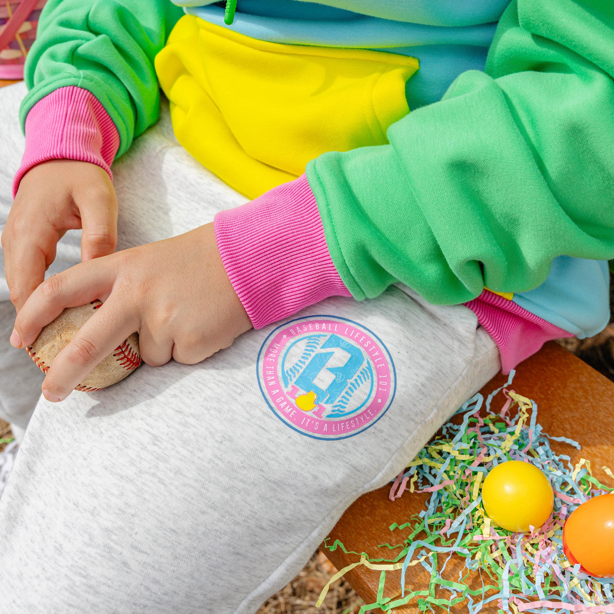 Person wearing colorful hoodie with a BL101 logo on grey sweatpants, surrounded by Easter eggs and grass.