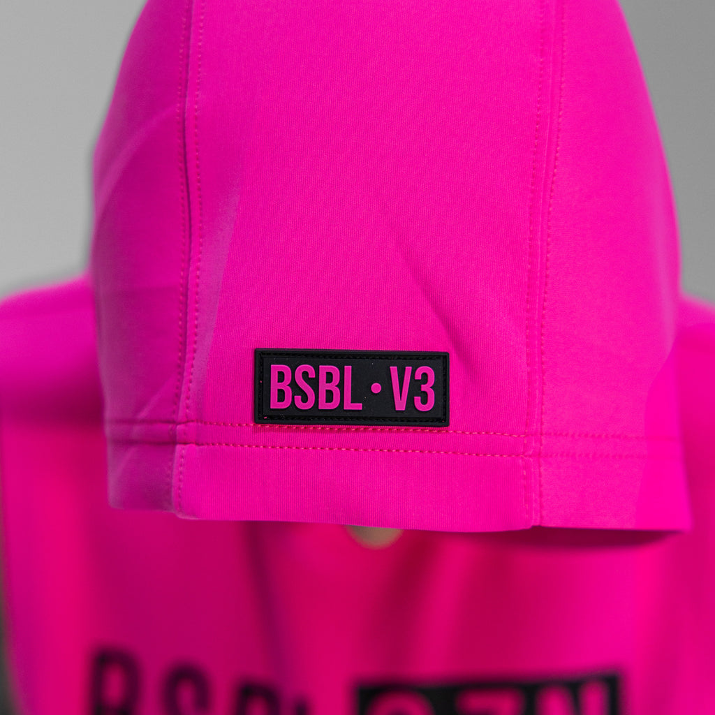 Close-up of a bright pink hoodie with a black label reading 'BSBL V3' on a gray background.