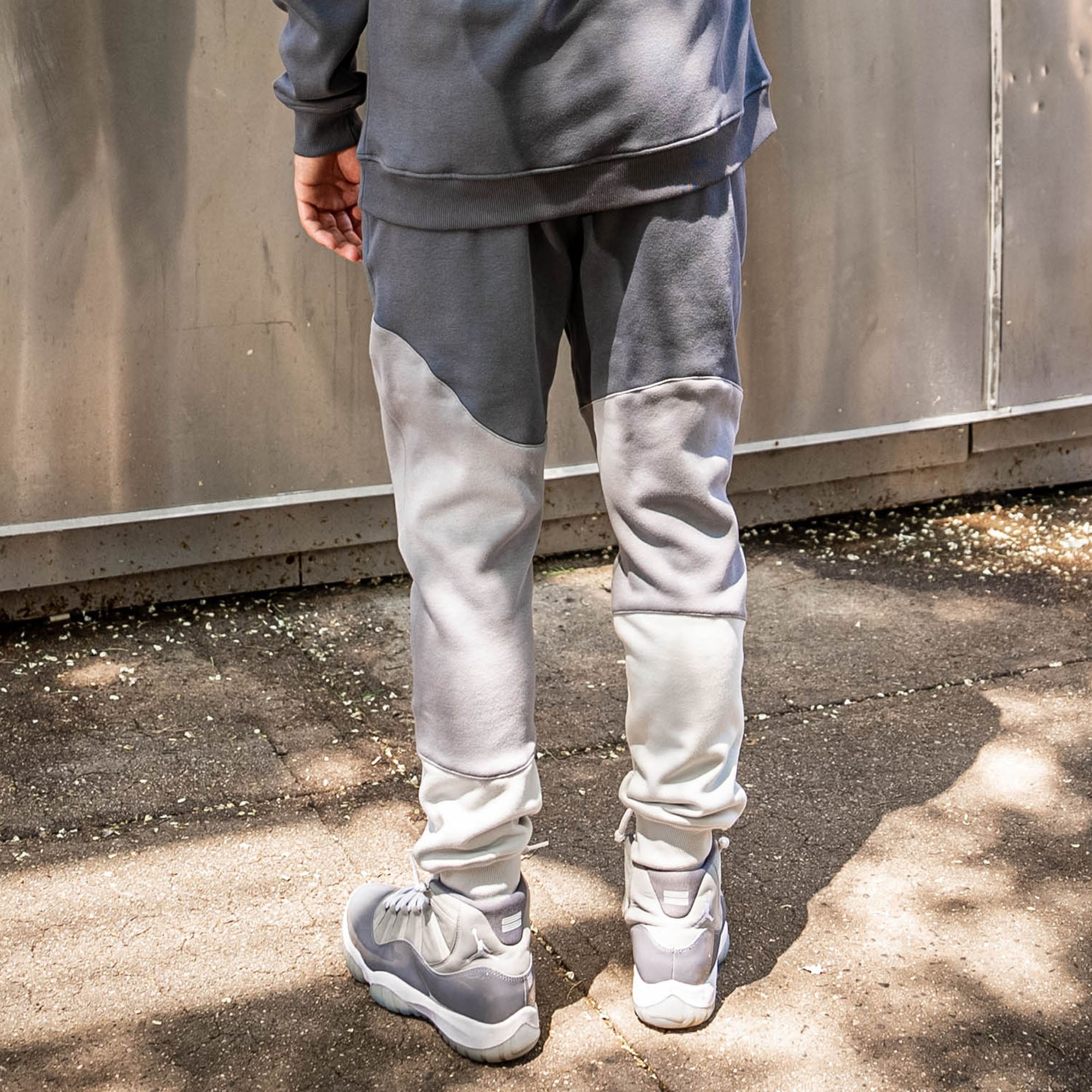 Person wearing a gray and white tracksuit with gray sneakers standing on a concrete surface.