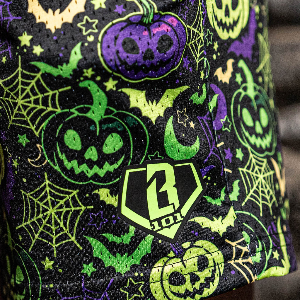 Purple and green halloween-themed shorts with pumpkins, bats, and webs on a black background.