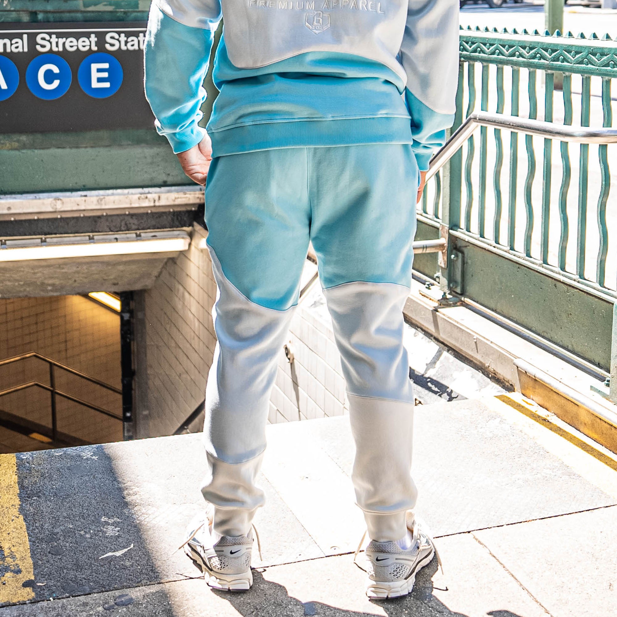 Person wearing light blue and white color-blocked sweatpants in front of subway entrance