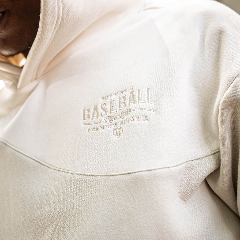 Close-up of a beige hoodie with a 'Authentic Baseball Lifestyle PREMIUM APPAREL' logo on the chest.