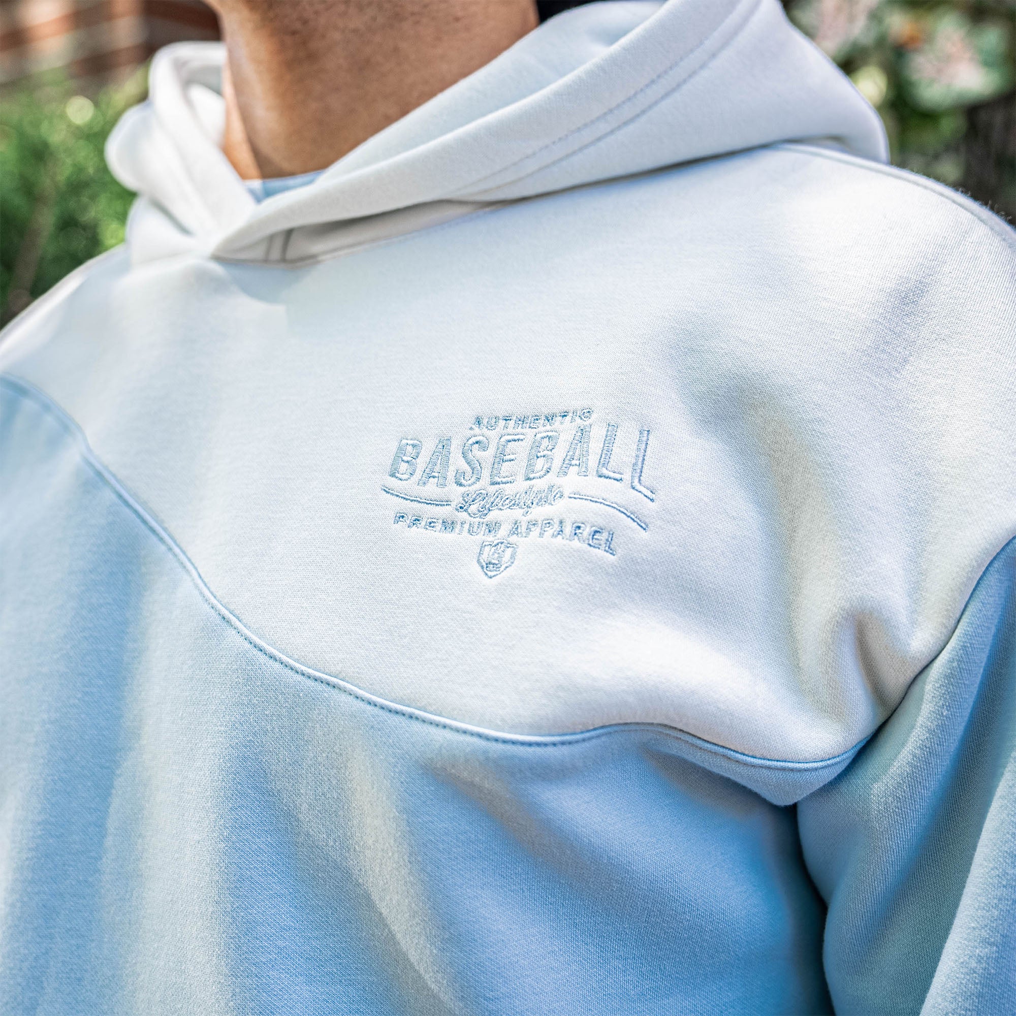Light blue hoodie with 'Authentic Baseball Lifestyle PREMIUM APPAREL' text on a blurred background