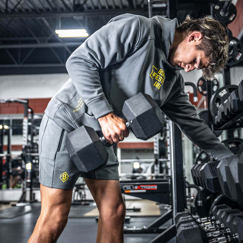 Man lifting dumbbells wearing a gray BL101 hood with yellow logo in a gym setting