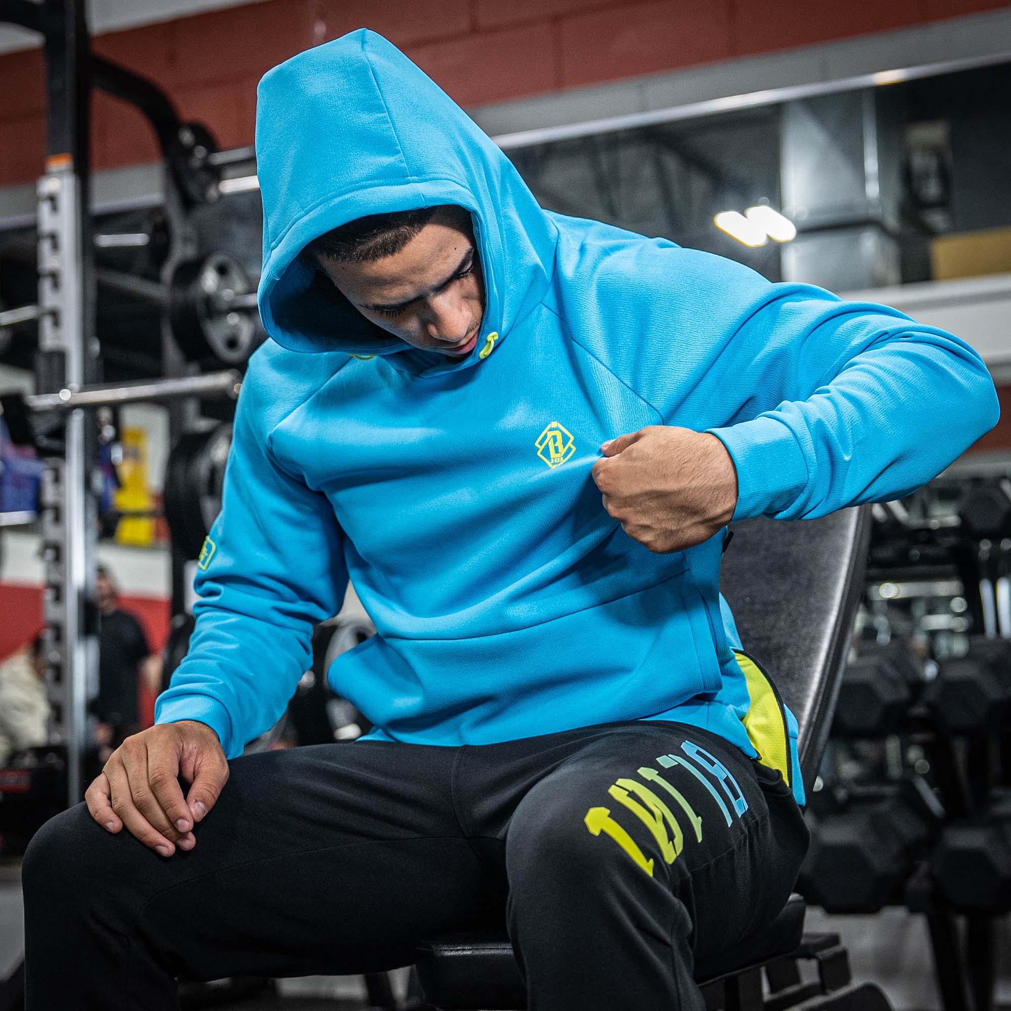 Person wearing a bright blue hoodie with a yellow BL101 logo in a gym setting