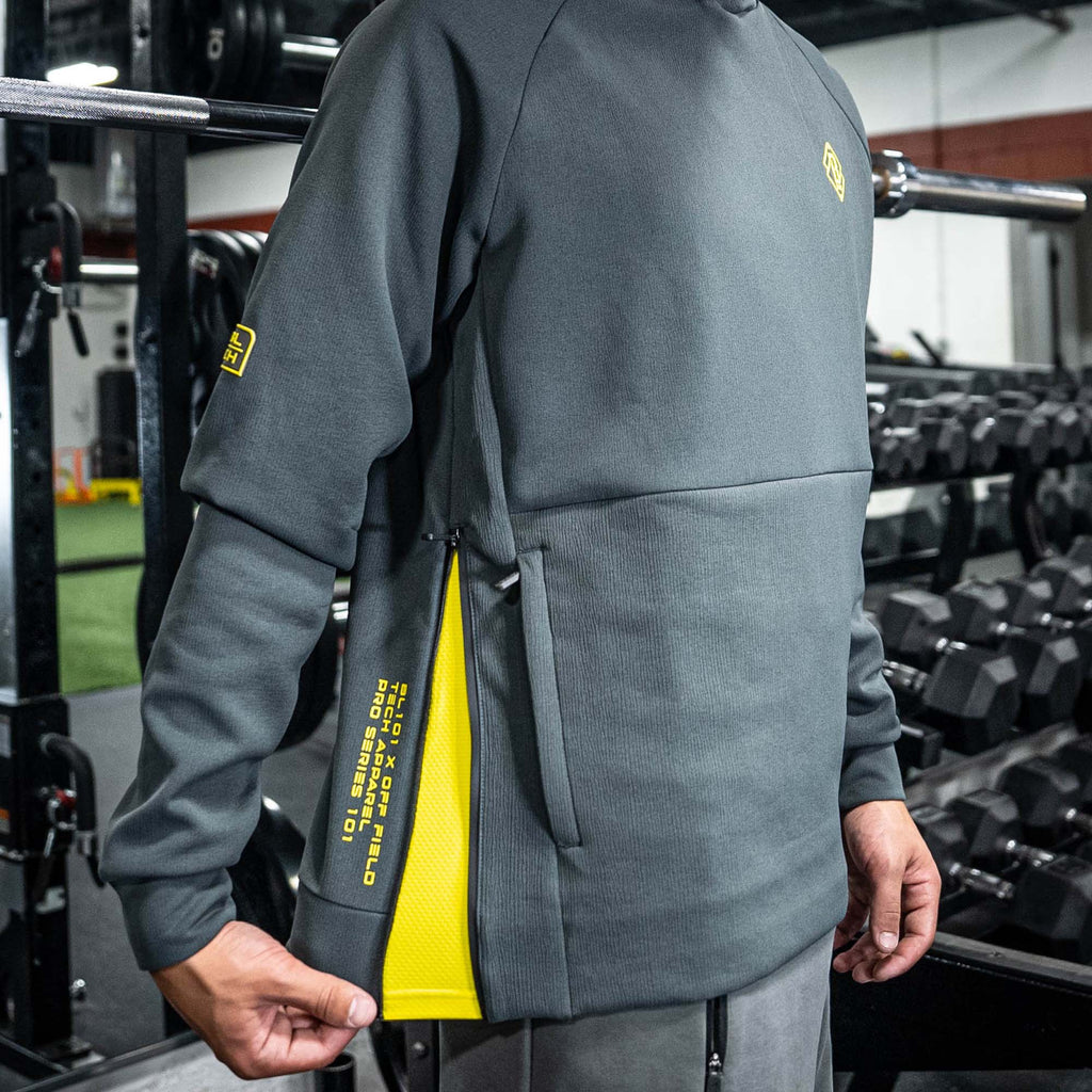 Person wearing a gray BL101 hoodie with yellow accents in a gym setting