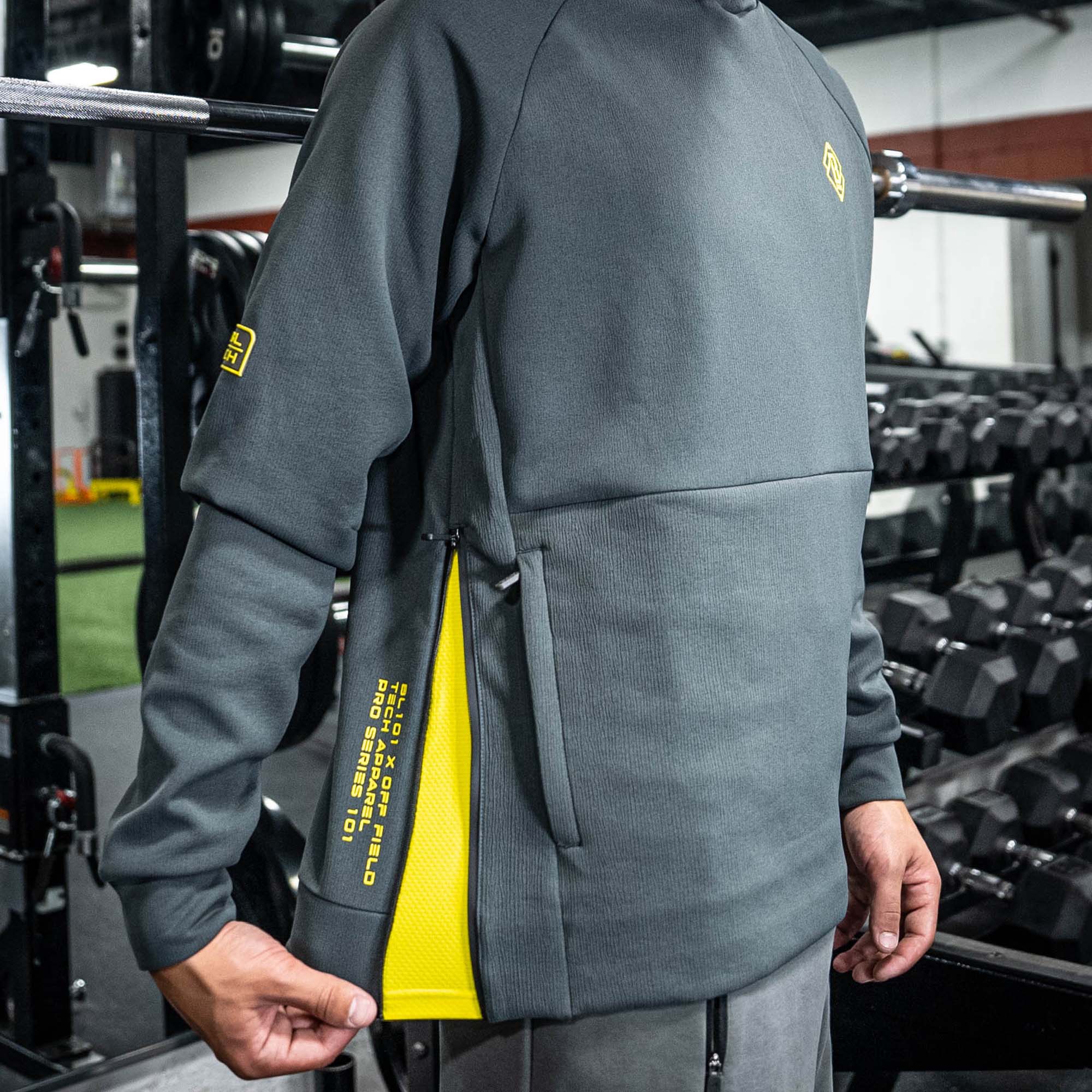 Person wearing a gray BL101 hoodie with yellow accents in a gym setting