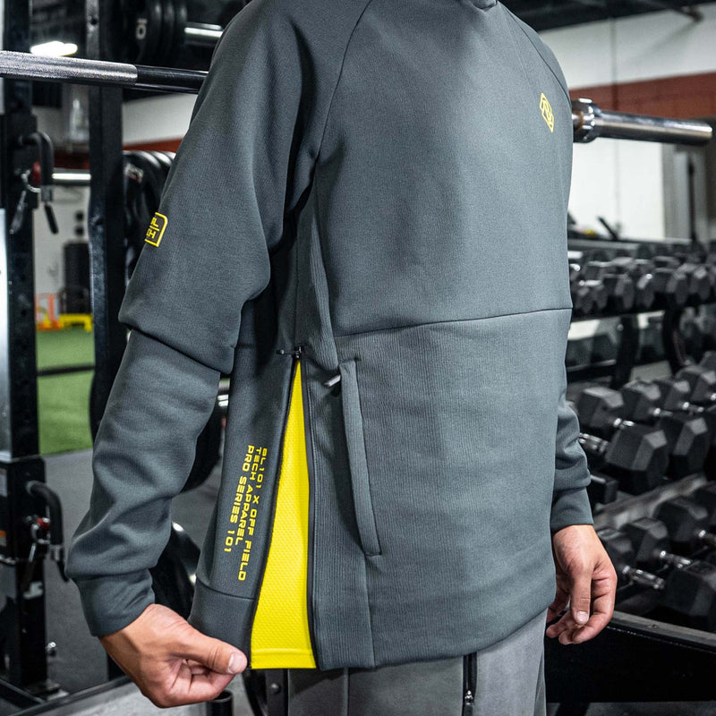 Person wearing a gray BL101 hoodie with yellow accents in a gym setting