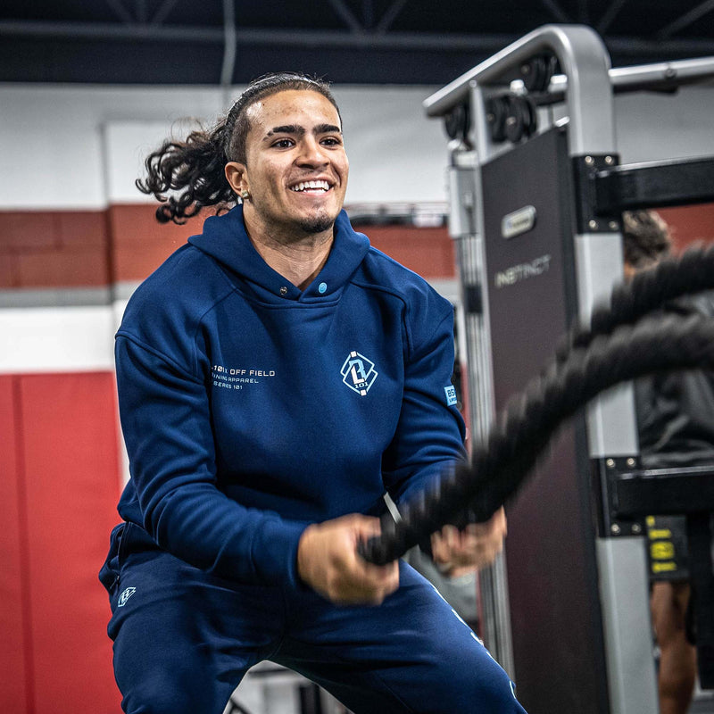 Person wearing a blue hoodie with a BL101 X OFF FIELD logo, using gym equipment in a gym setting.