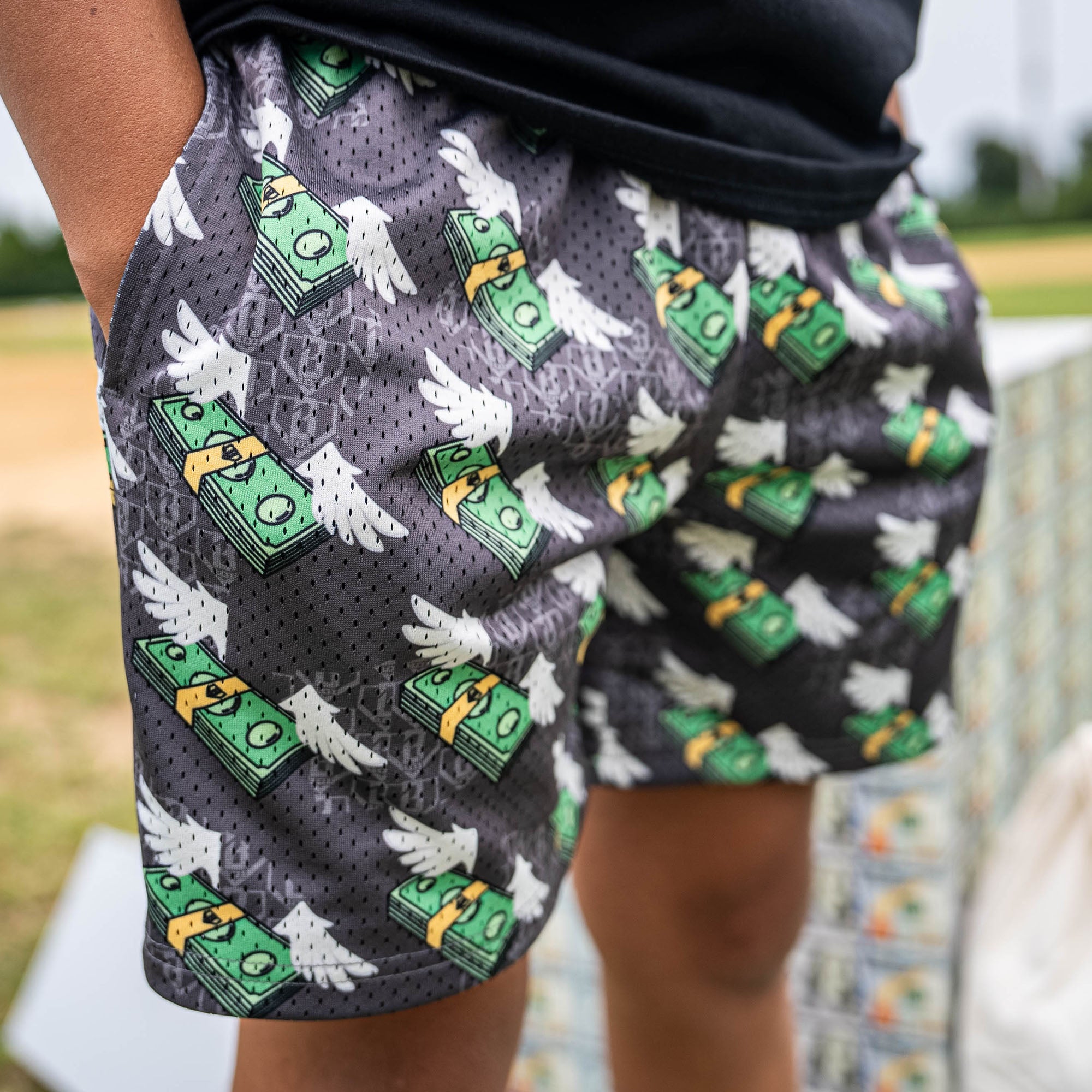 Person wearing gray shorts with green and white money with wings pattern 