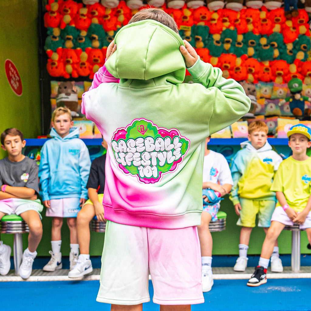 Person wearing a gradient green and pink hoodie with 'Baseball Lifestyle 101' text in front of a colorful wall.