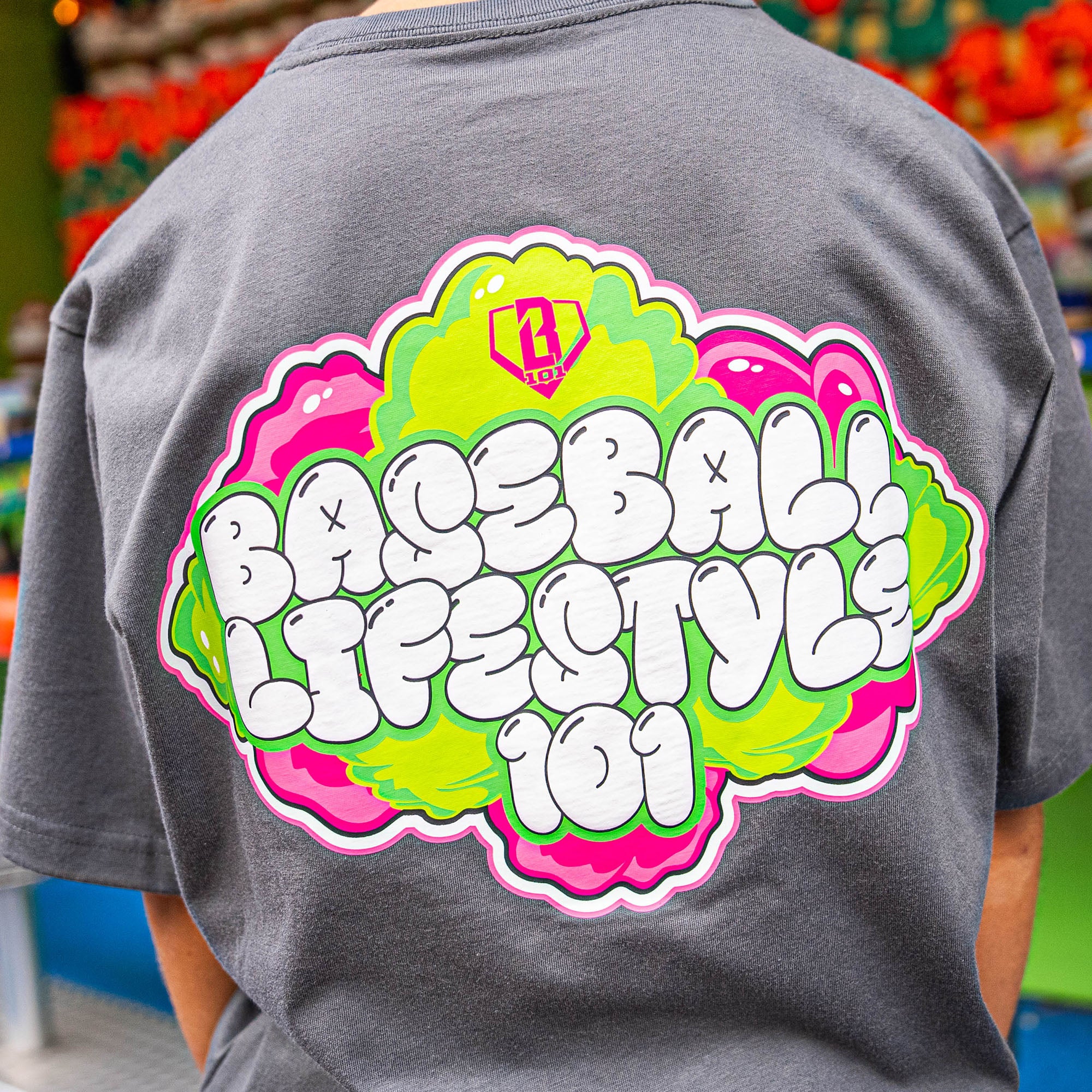 Gray t-shirt with pink and green 'Baseball Lifestyle 101' graphic on the back