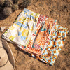 Three pairs of patterned shorts on a sandy surface with a hat nearby.