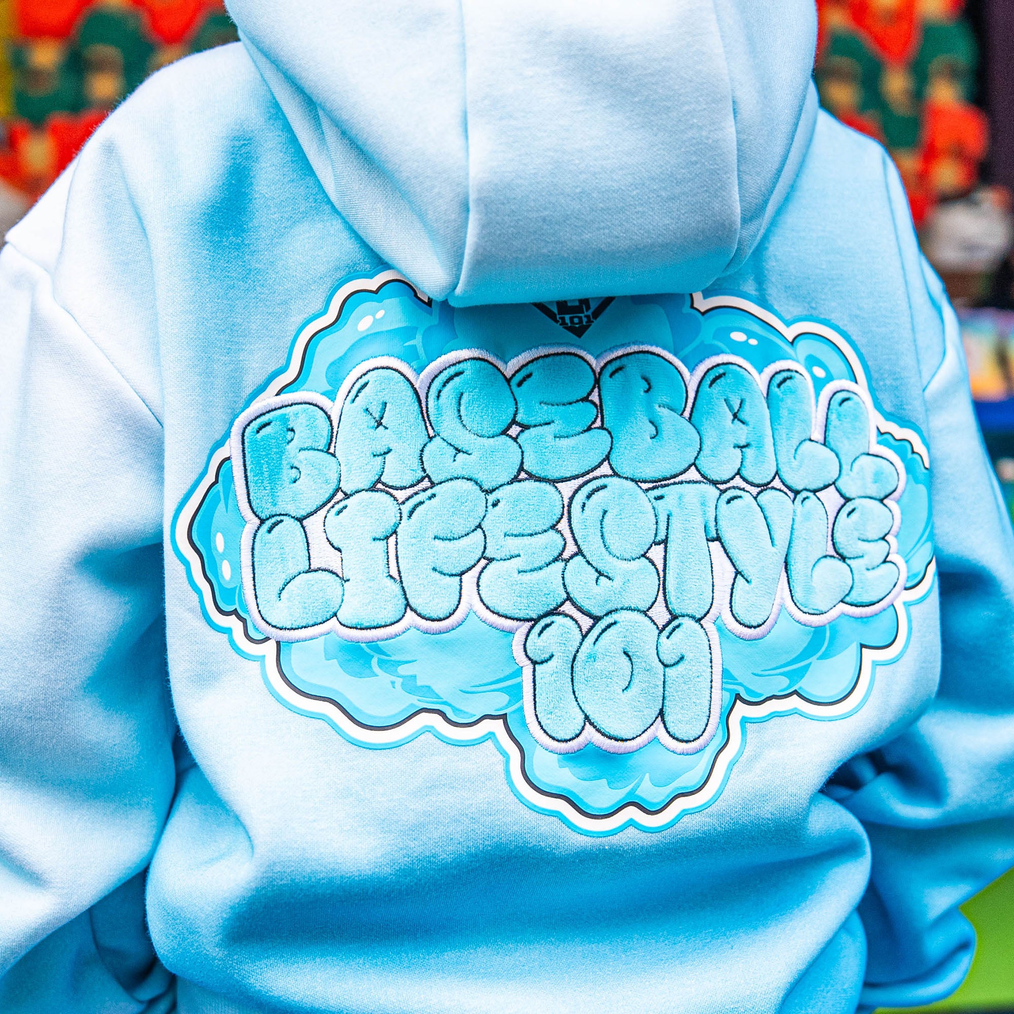 Light blue hoodie with 'BASEBALL LIFESTYLE' logo on the back, colorful background