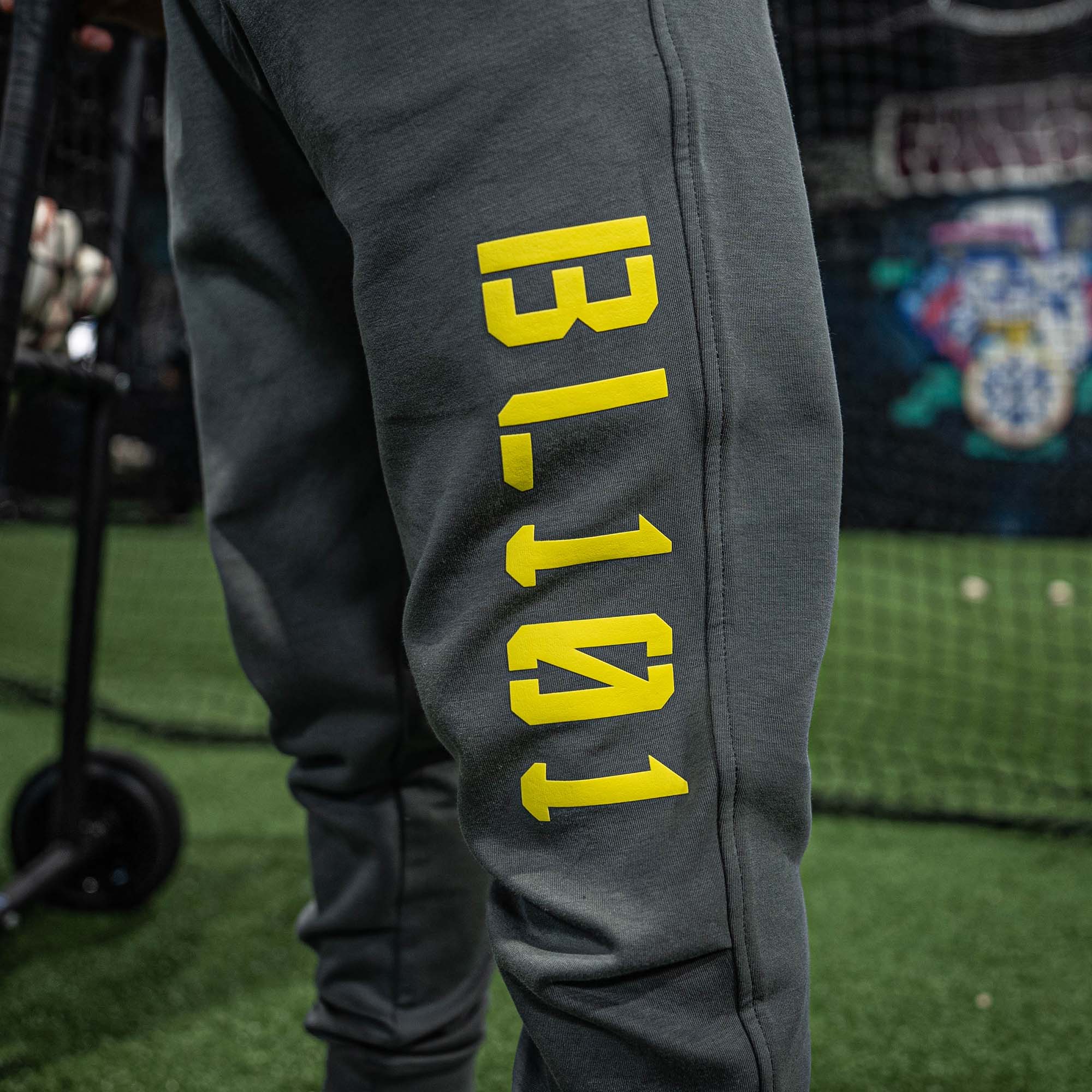 Gray sweatpants with yellow BL101 text on a grassy field background