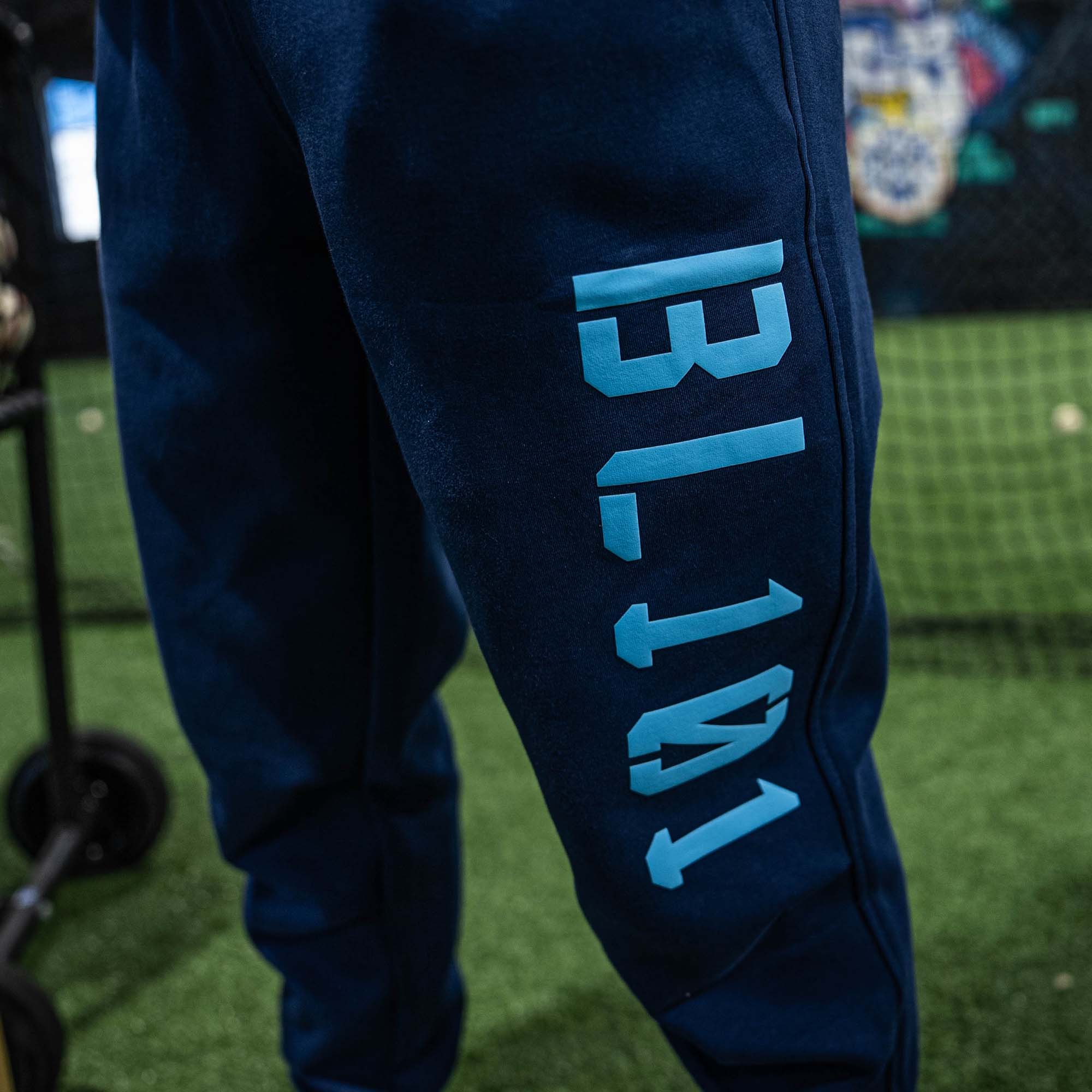 Close up of blue sweatpants with 'BL101' printed on them against a blurred sports field background